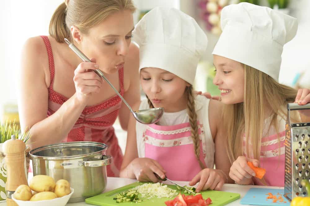 Girls with mother preparing delicious fresh salad in the kitchen