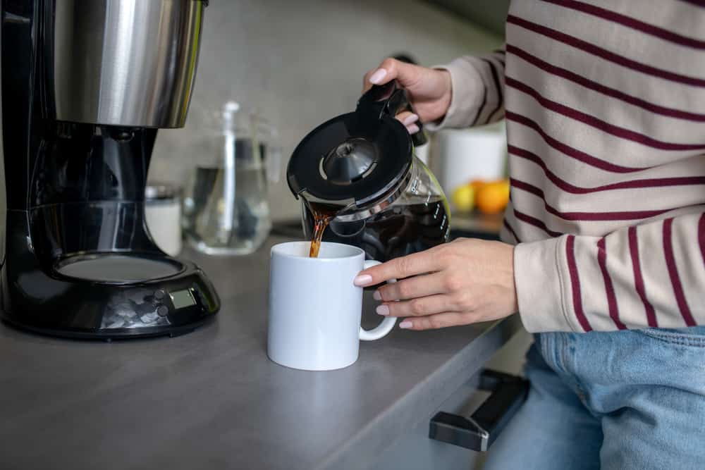 Indoors. Woman hands pouring coffee from coffee jug into white cup