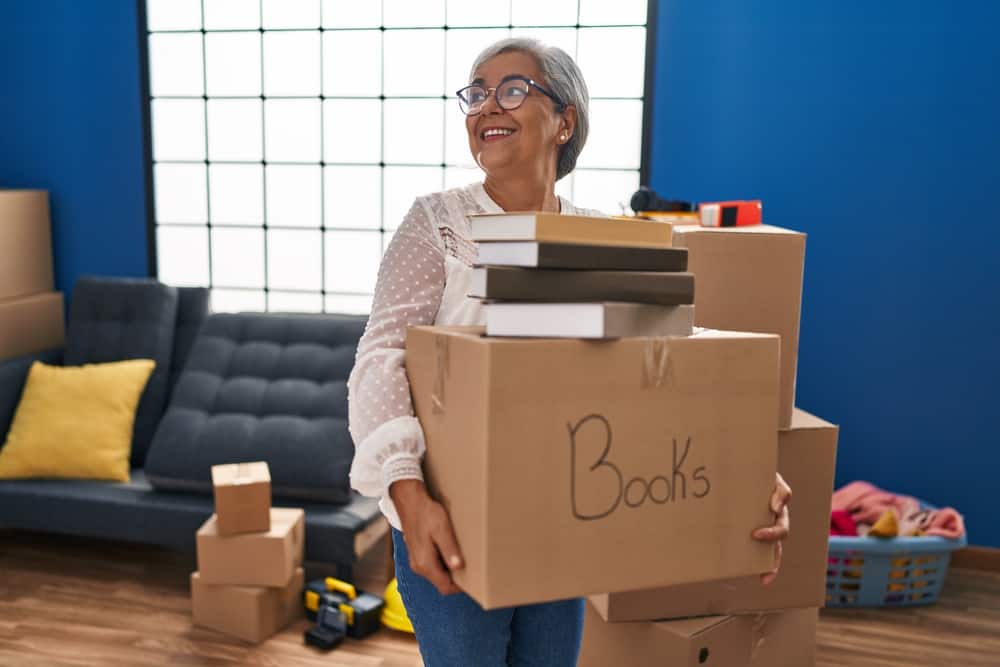 Middle age woman smiling confident holding books package at new home