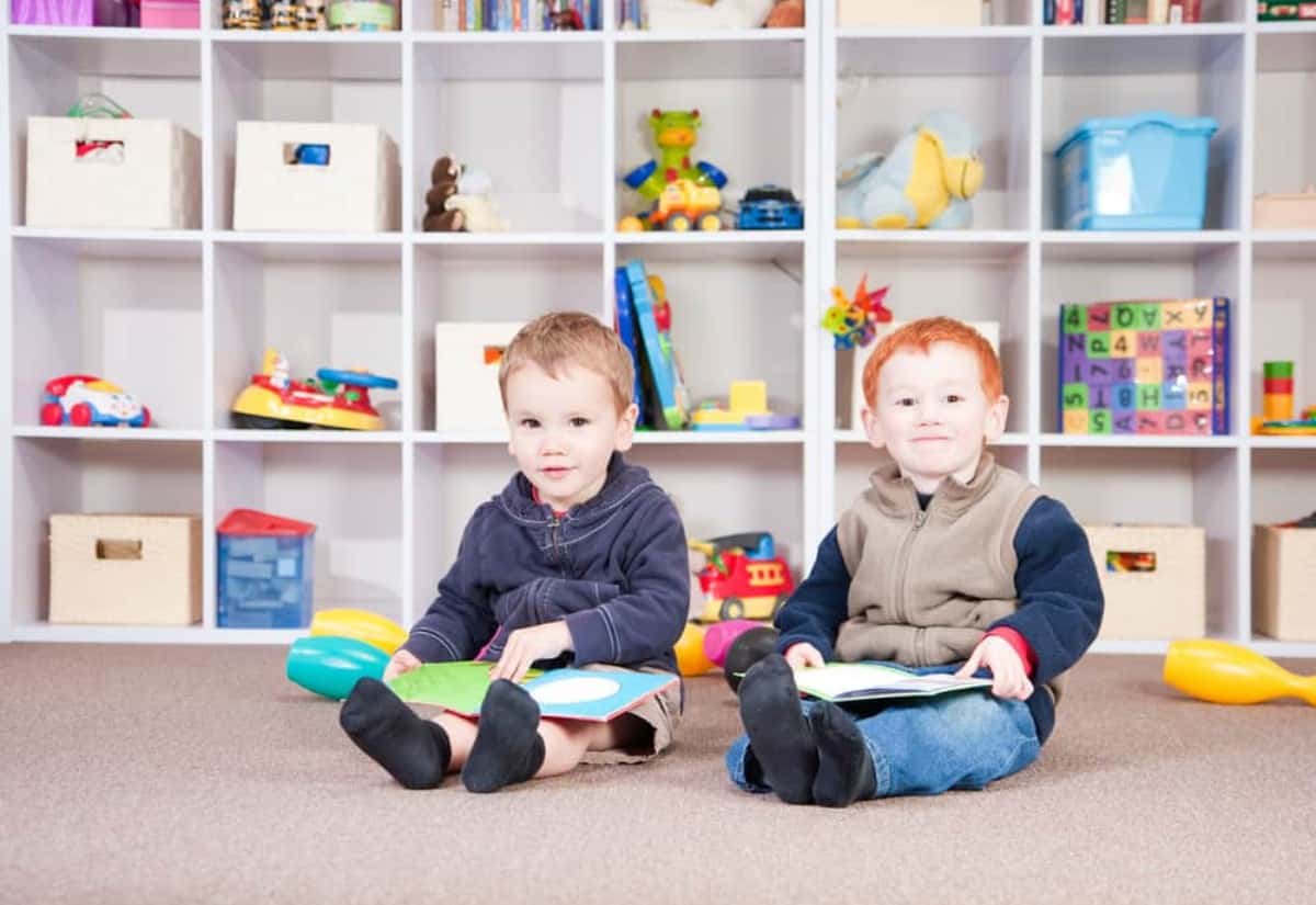 Two smiling boys reading books in play room.