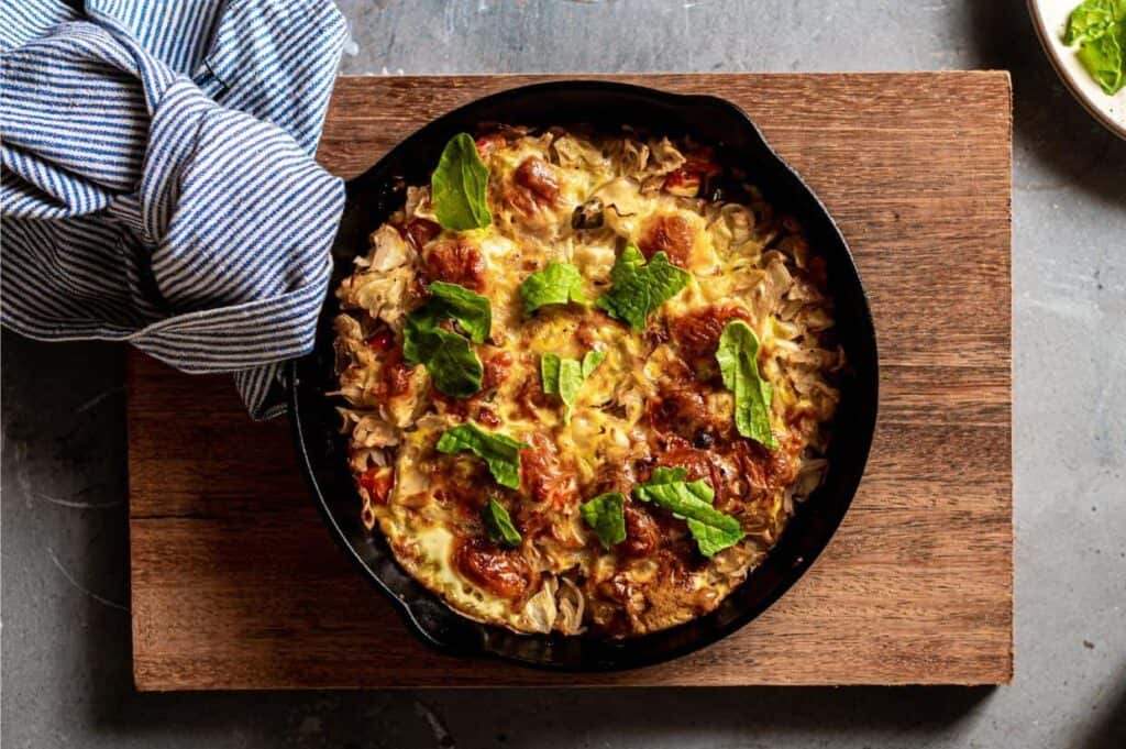 Breakfast frittata baked in cast iron skillet with kitchen towel around handle.