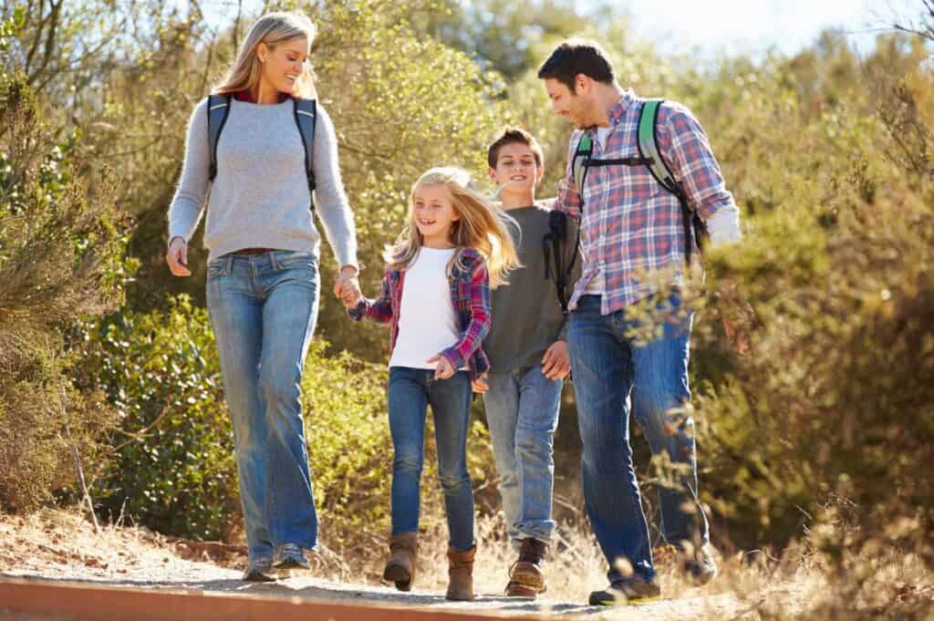 Family hiking in countryside wearing backpacks.