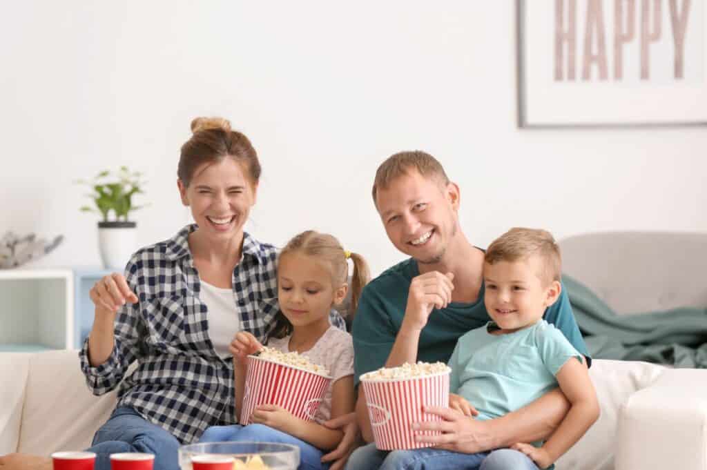 Happy family eating popcorn while watching TV at home.