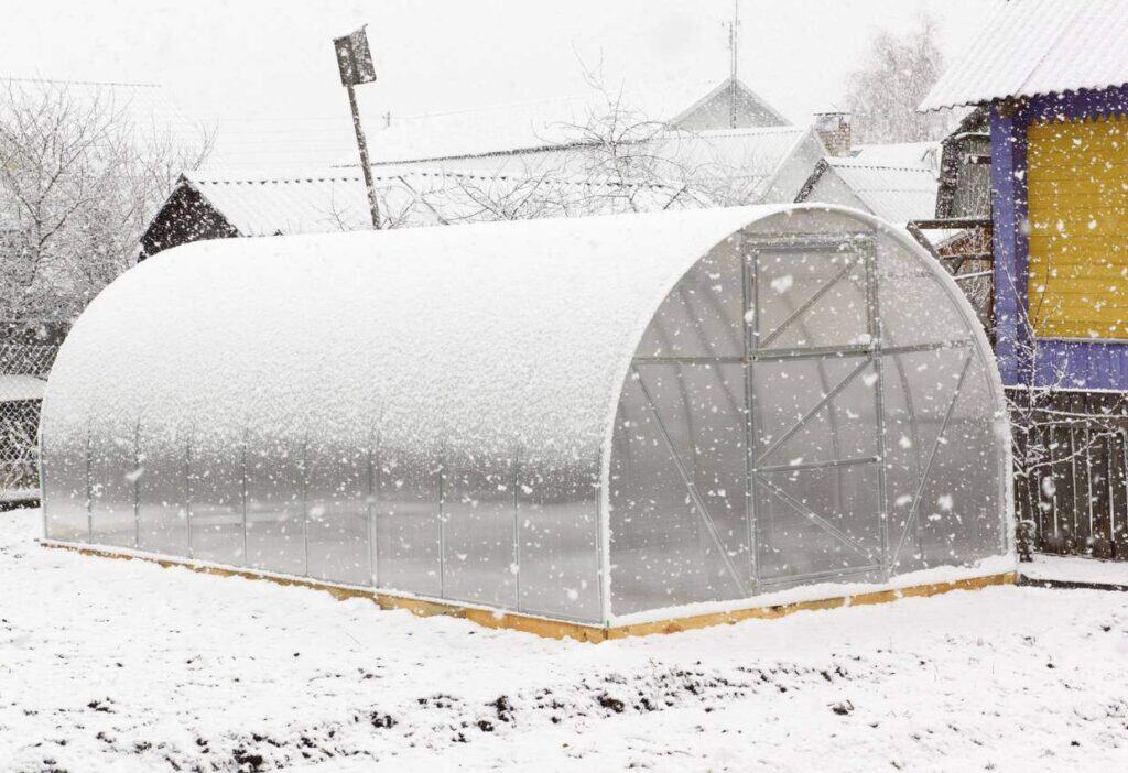 A greenhouse covered in snow on a snowy day.