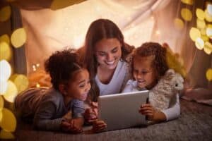 Mother with two girls watching family camping movies on a tablet in a tent.