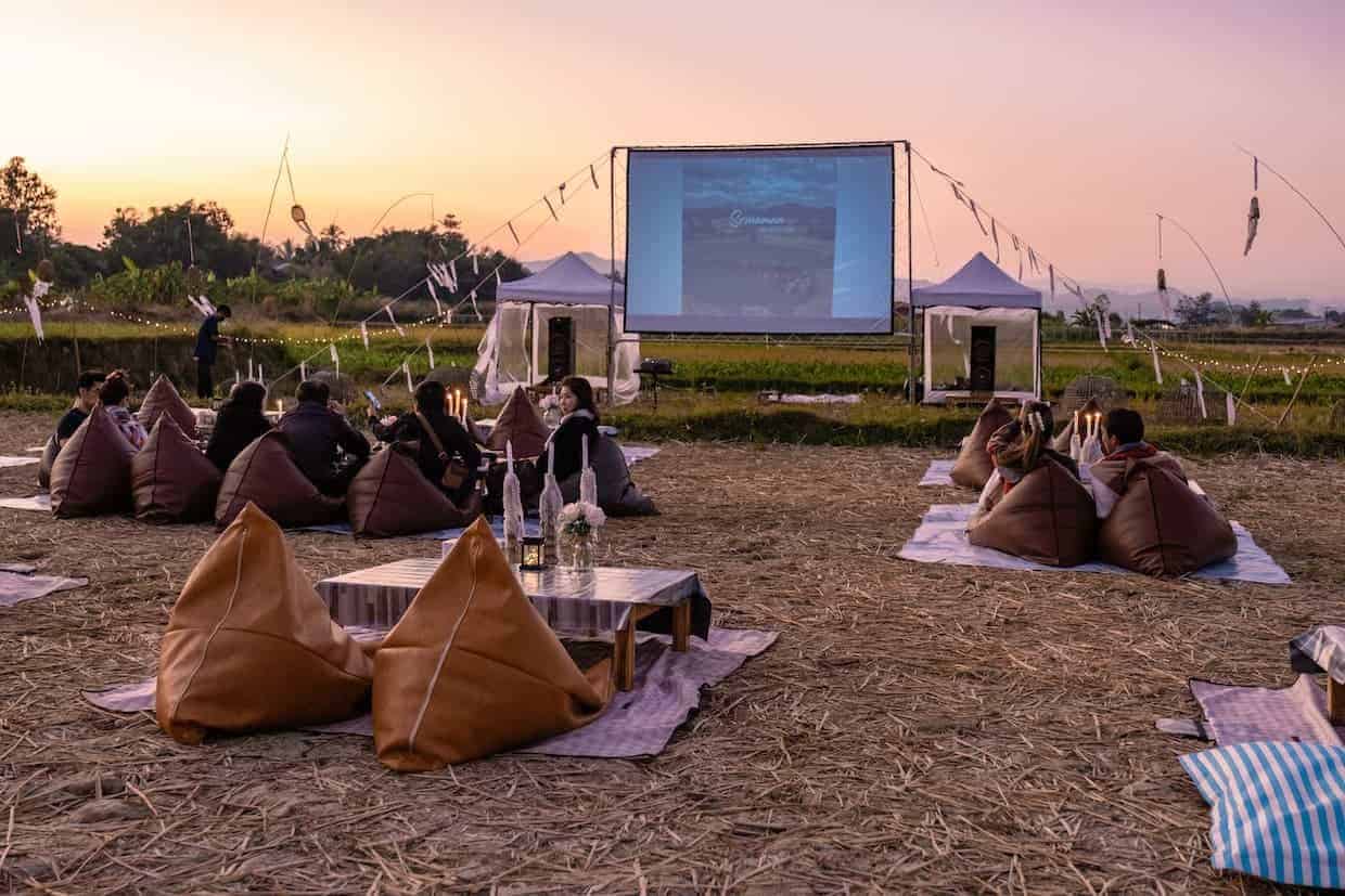 Outdoor cinema setting with pillows and blankets and small tables.