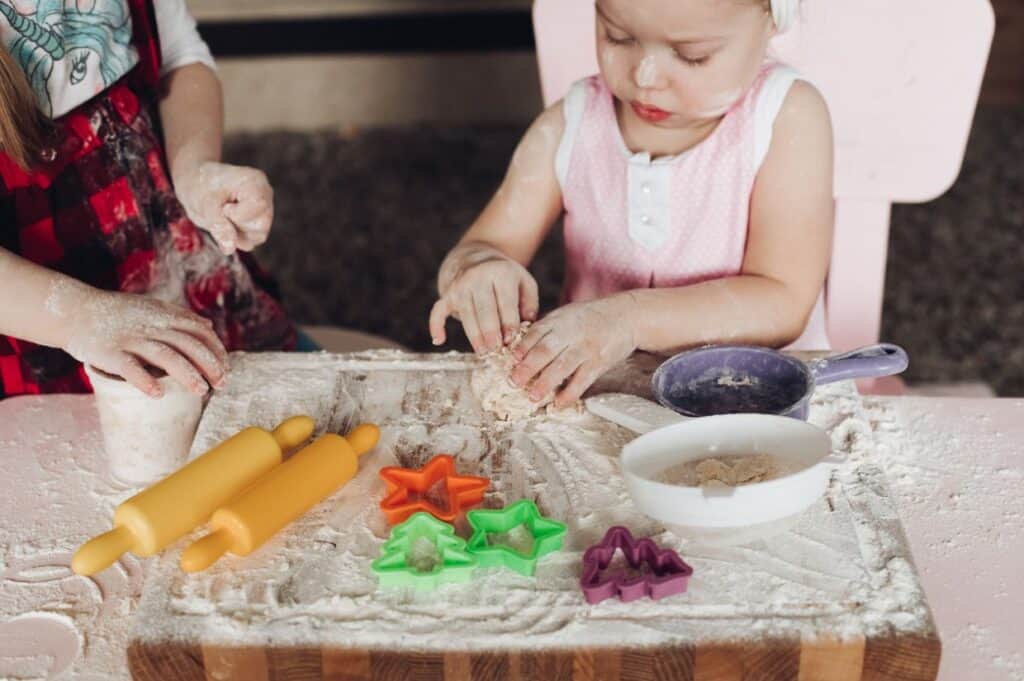 Two young children are playing with flour and dough at a kitchen table.