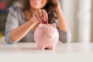 A woman smiles as she places a coin into a pink piggy bank, symbolizing saving money and financial responsibility.